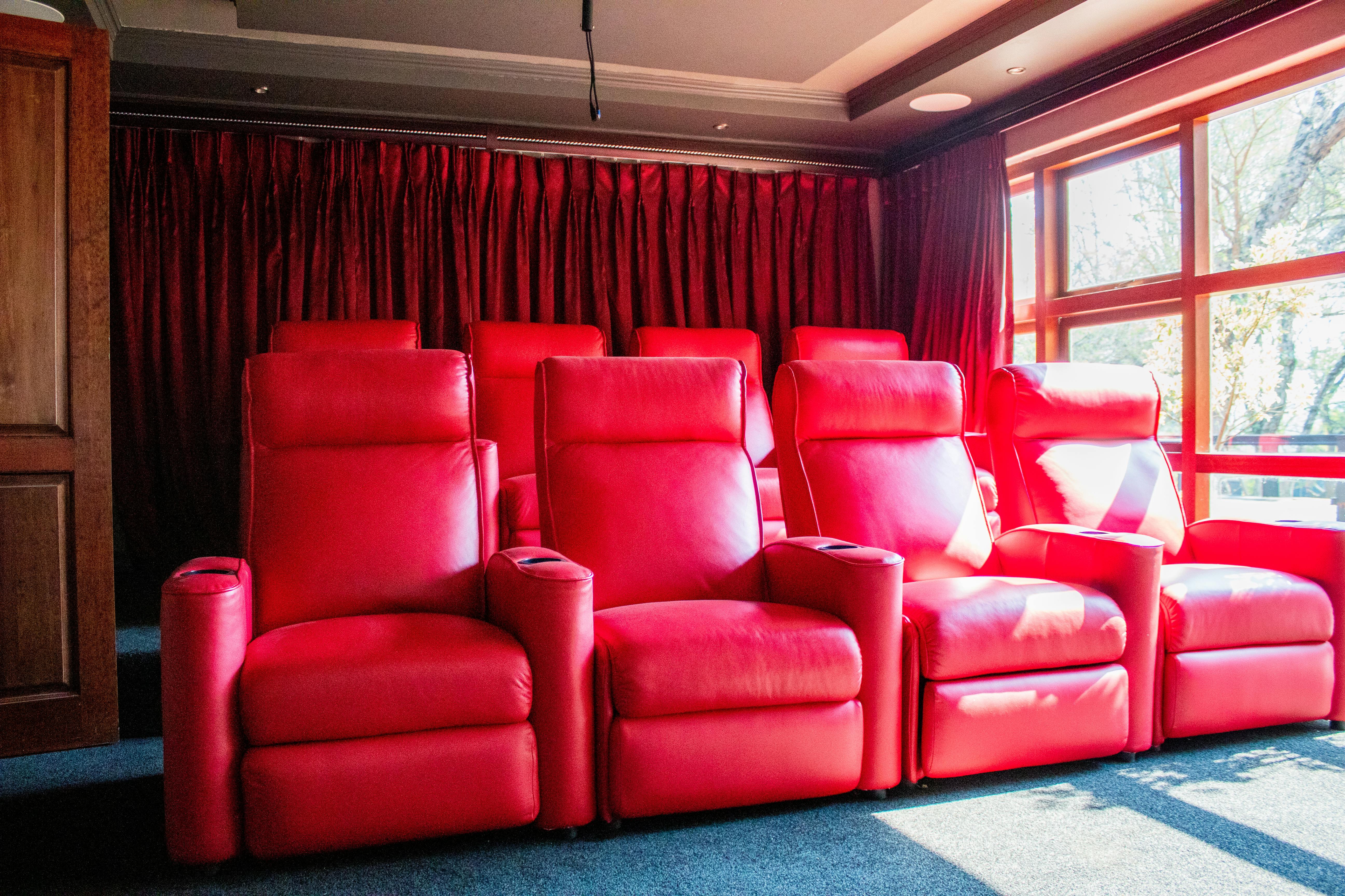 Elegant home theater featuring vibrant red leather reclining chairs and natural light.